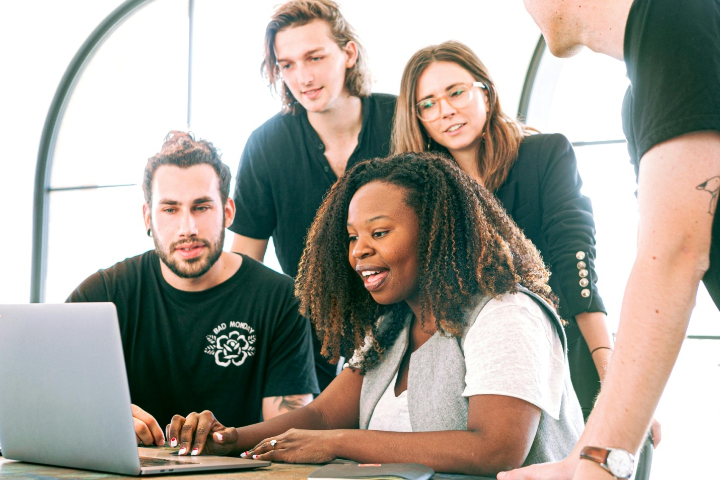 5 people in an office are looking at a laptop