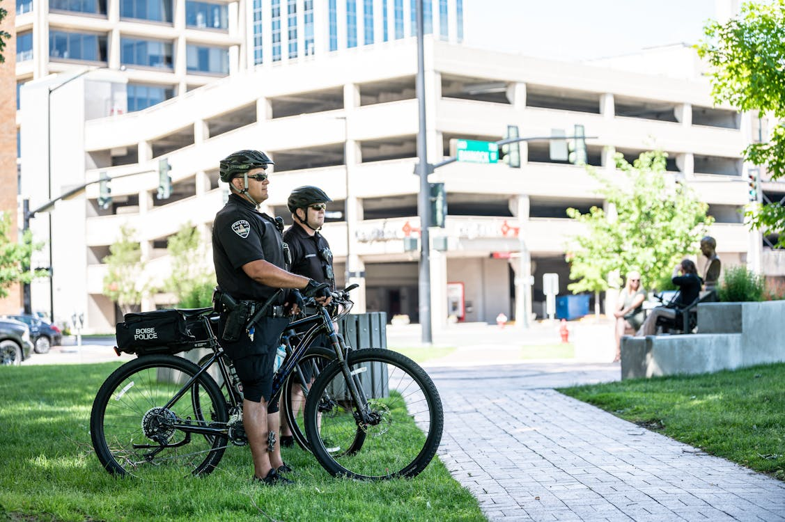 Two security professionals with bicycles standing on the lawn in an urban district in front of a business building