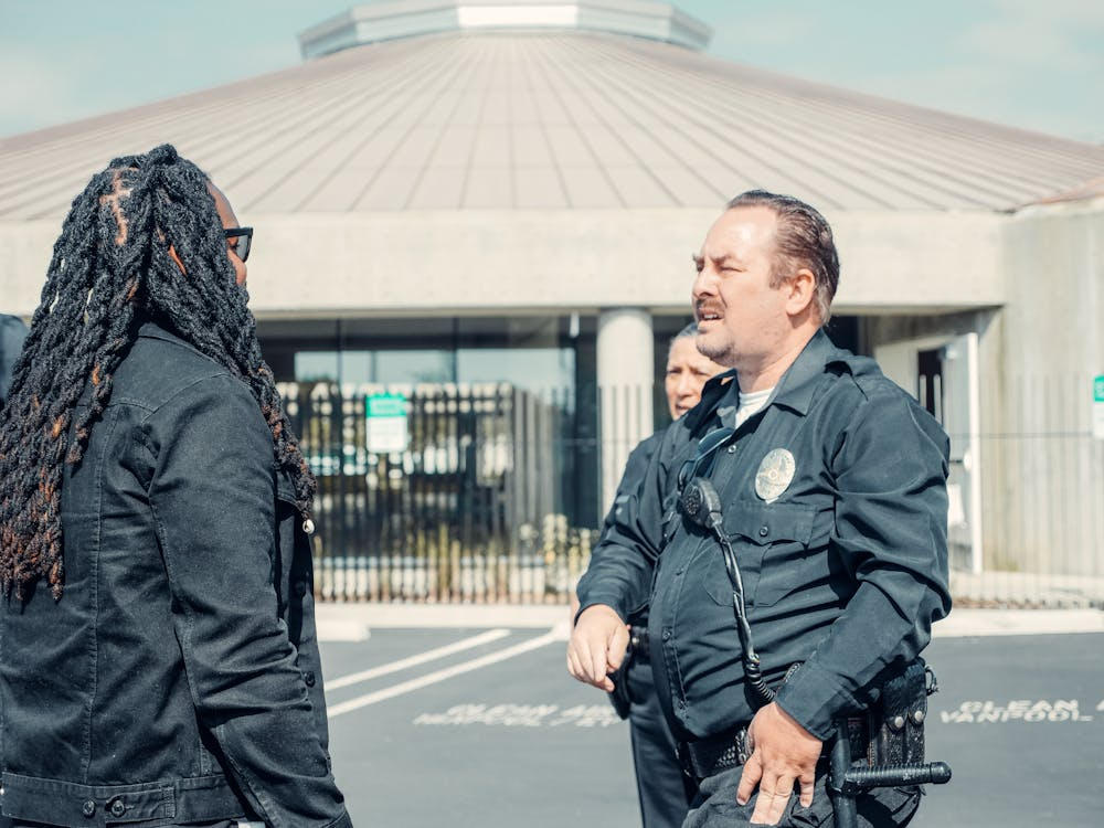 Two security professionals talking to a man in dreadlocks wearing a black jacket