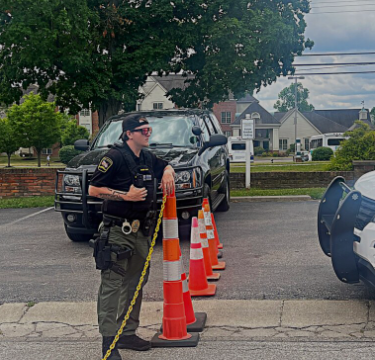 An armed officer standing next to a traffic cone.