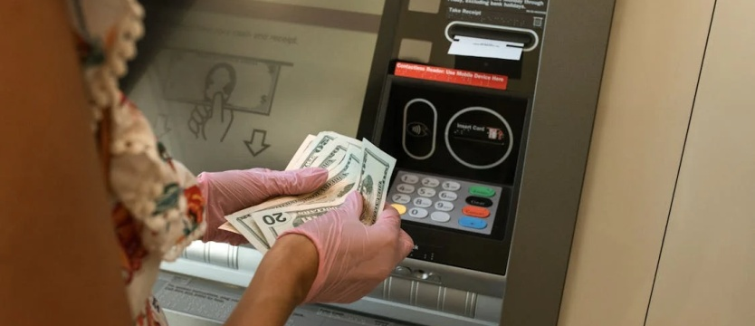 An image of a person counting money in front of an ATM