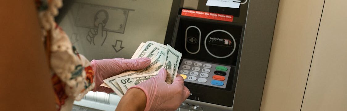 Person counting money in front of an ATM during a cash withdrawal