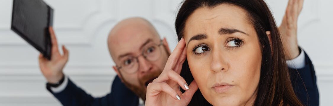 Man aggressively shouting behind a distressed woman in a workplace environment, indicating a potential threat situation.
